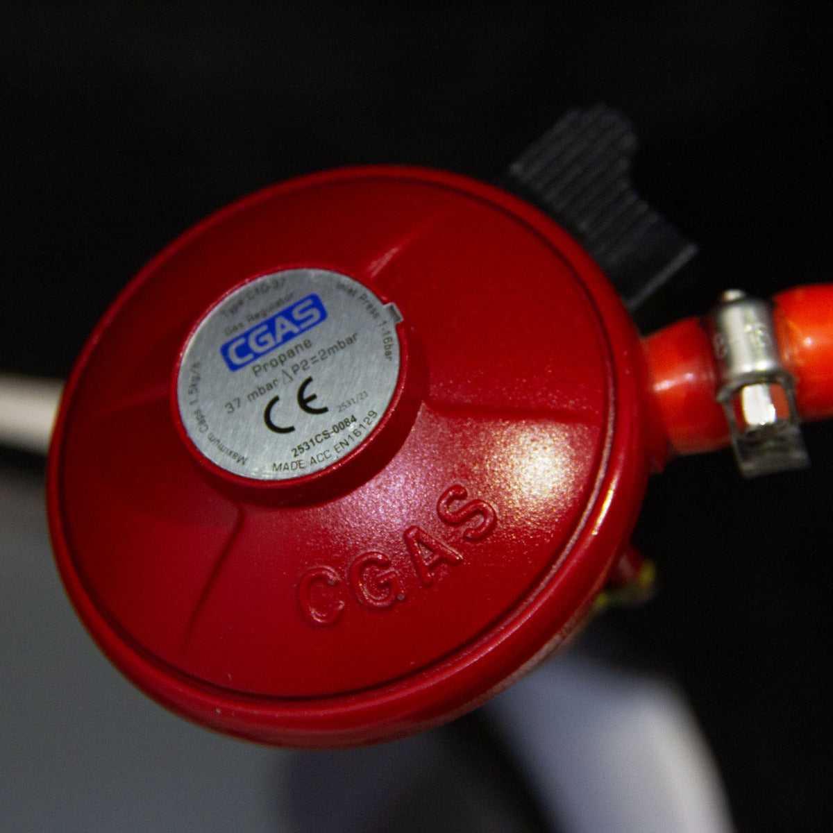 Regolatore di gas rosso brillante con etichetta CGAS, progettato per bracieri a gas, con tubi metallici e dettagli robusti