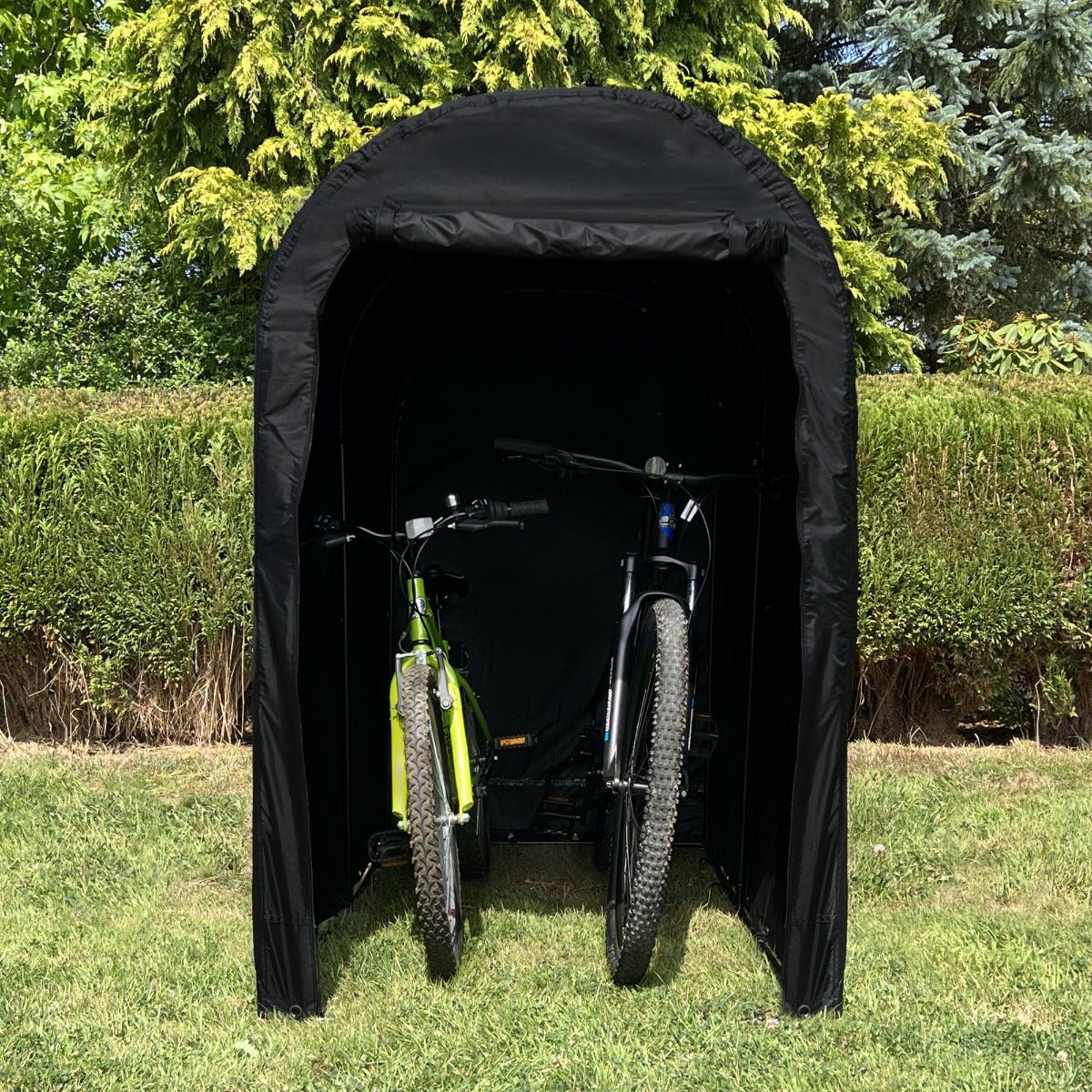 Tenda per biciclette nera con forma ad arco, ripara due biciclette in un giardino verde, proteggendole dagli agenti atmosferici