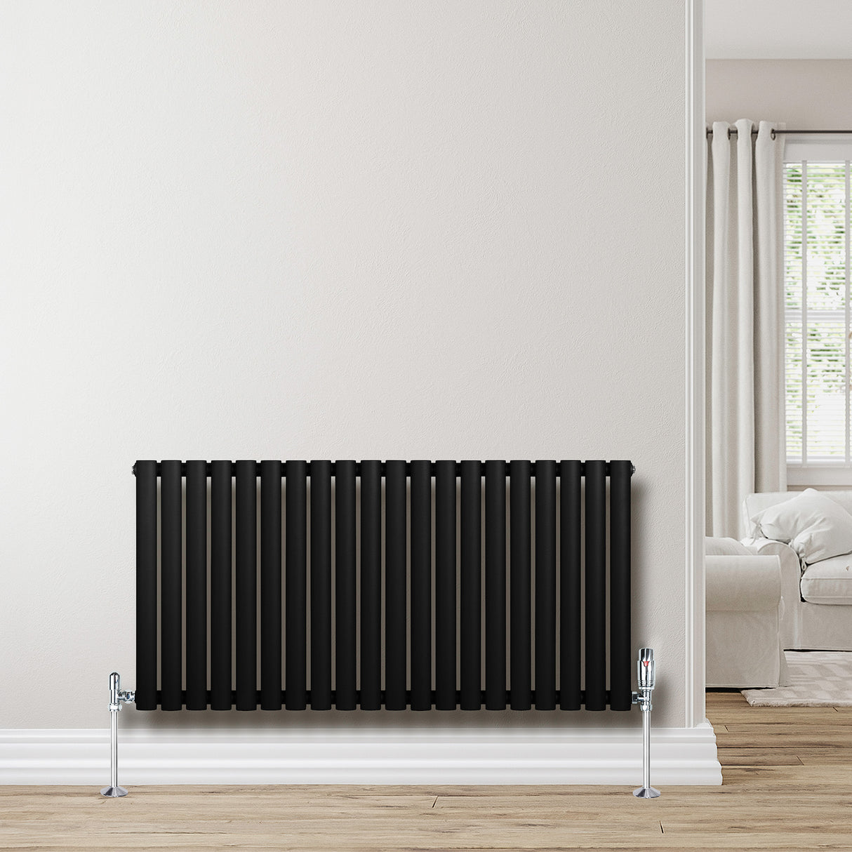 Radiatore ovale a colonna singola orizzontale, finitura nera opaca, con valvole, installato su parete chiara in un ambiente luminoso