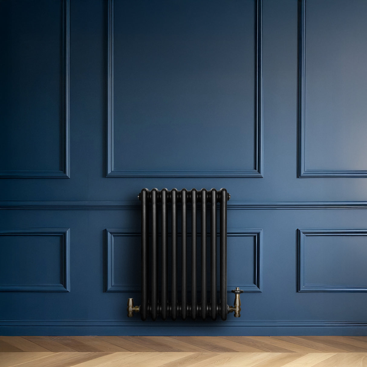 Radiatore tradizionale a 4 colonne in nero, installato su parete blu, con valvole in ottone e pavimento in legno chiaro