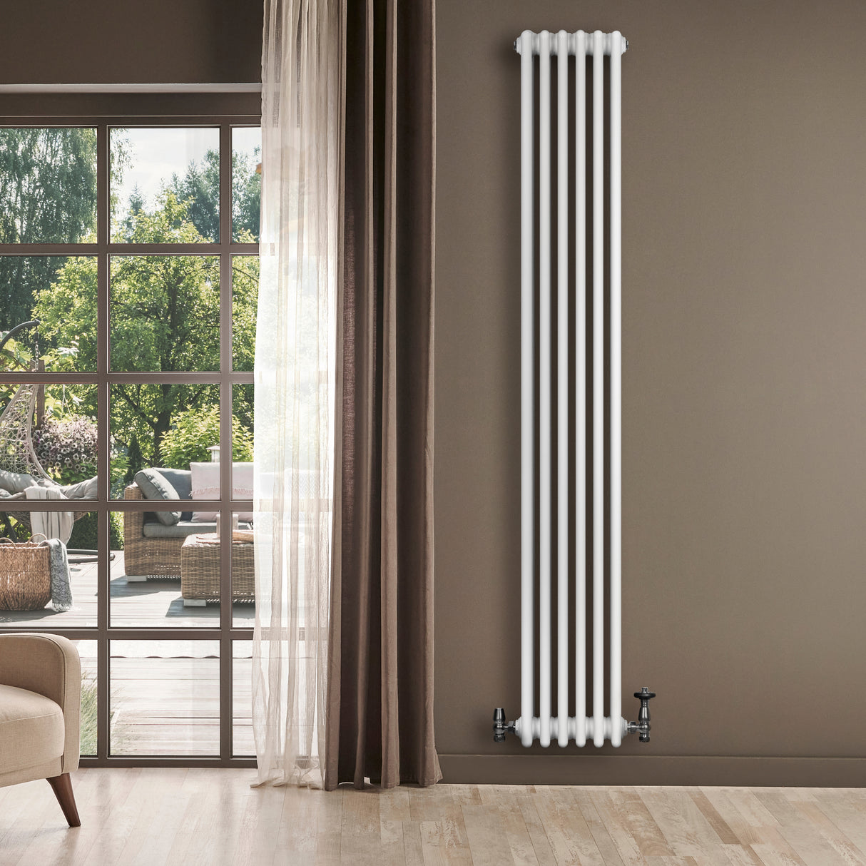 Radiatore tradizionale verticale a 4 colonne, finitura bianca, installato su parete, con valvole visibili e sfondo luminoso di un giardino