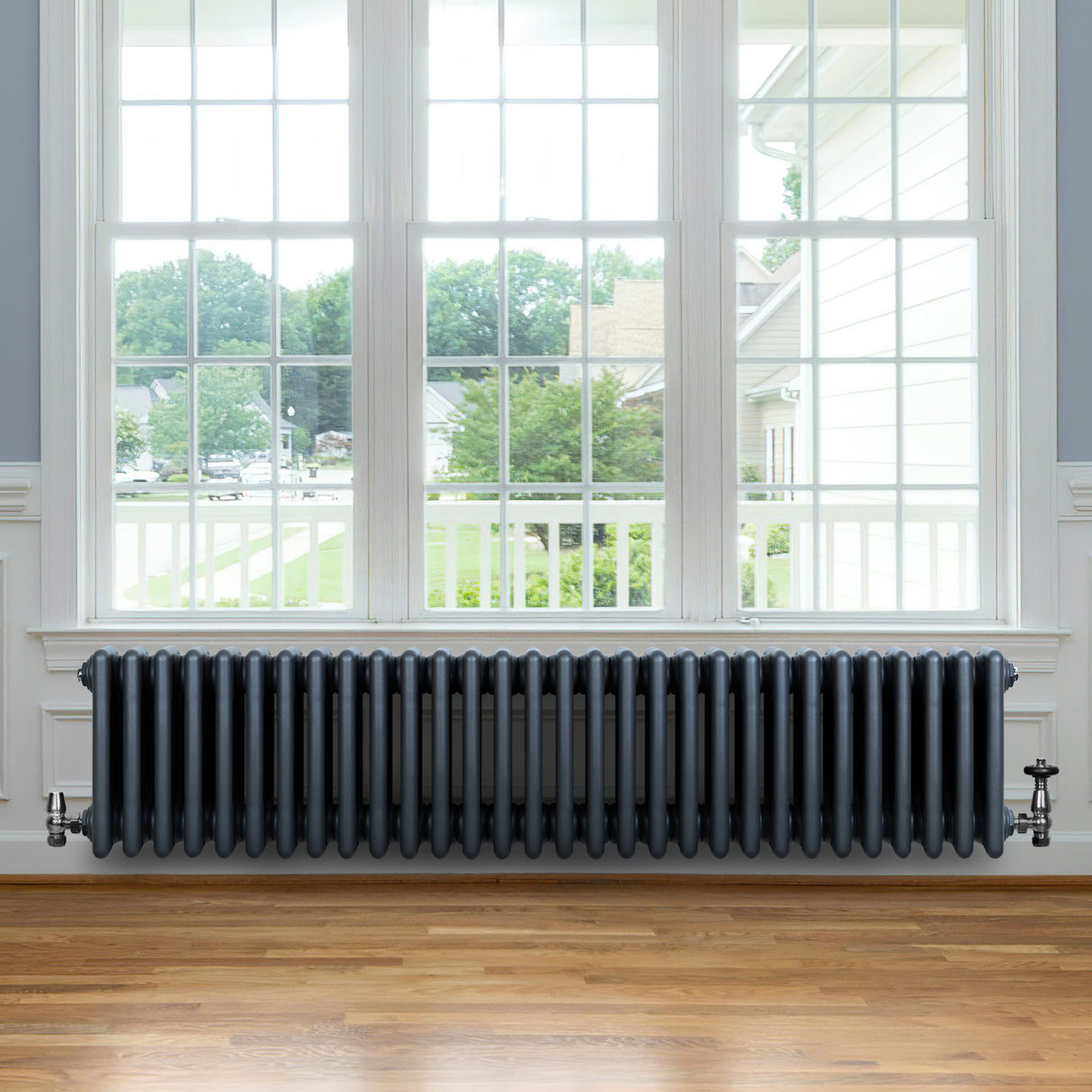 Radiatore tradizionale a 4 colonne in grigio antracite, con finitura liscia, posizionato sotto una grande finestra in legno chiaro