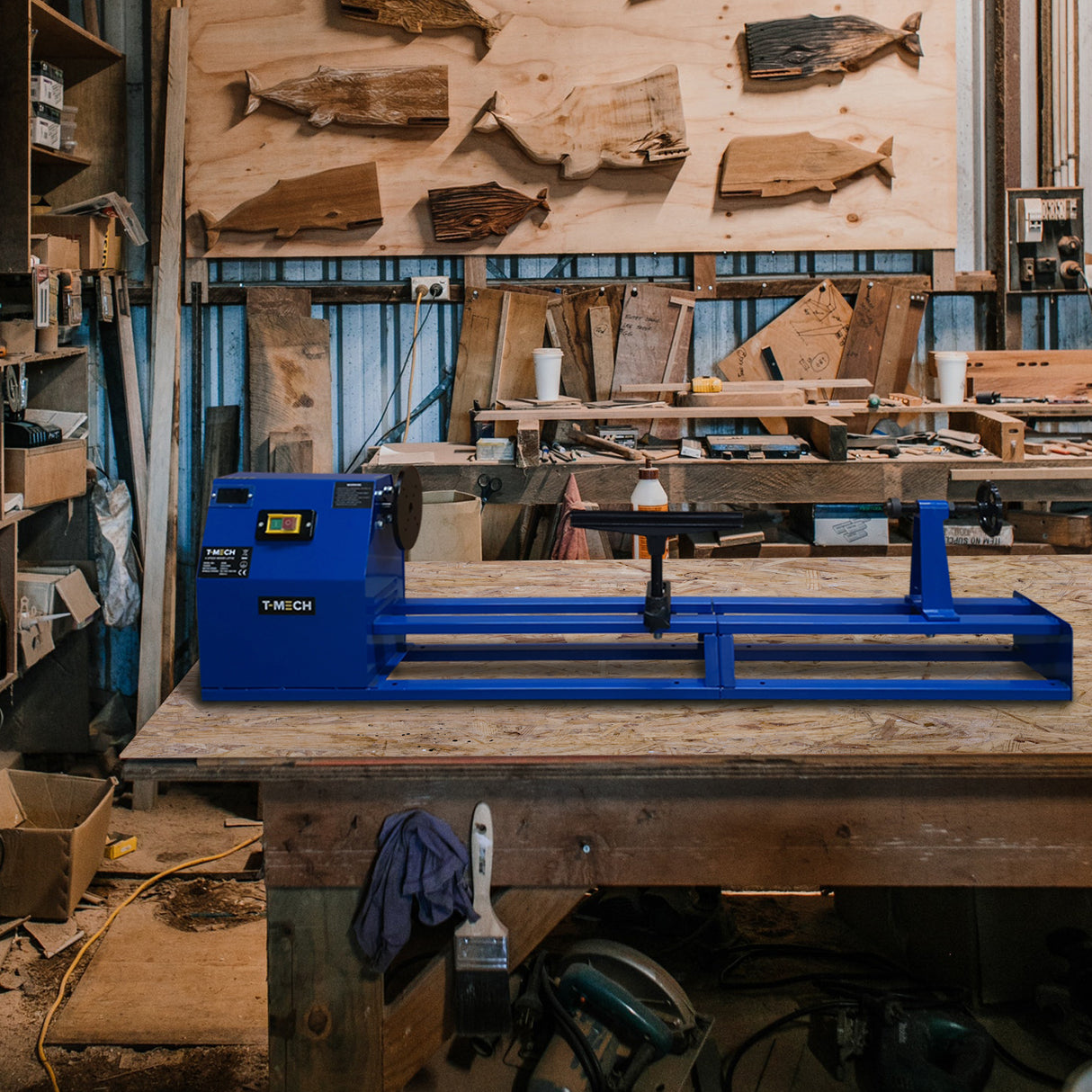 Tornio da legno T-Mech blu su un banco di lavoro in legno, circondato da attrezzi e pezzi di legno, ambiente di falegnameria rustico