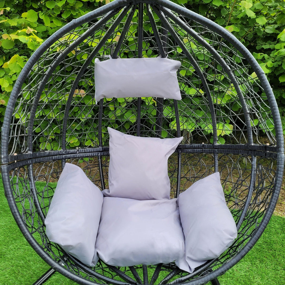 Sedia sospesa a uovo da giardino in rattan nero, con cuscini grigi morbidi, ideale per relax all'aperto in un ambiente elegante