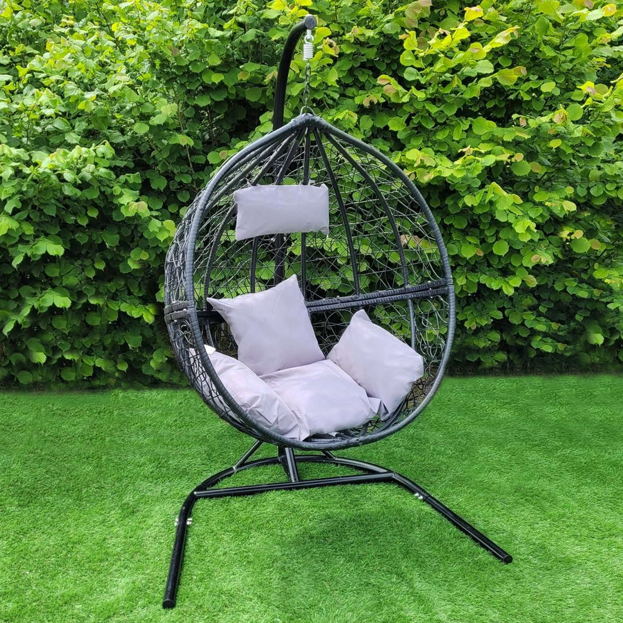 Sedia sospesa a uovo in rattan nero con cuscini bianchi, struttura metallica, ideale per giardini e spazi esterni eleganti