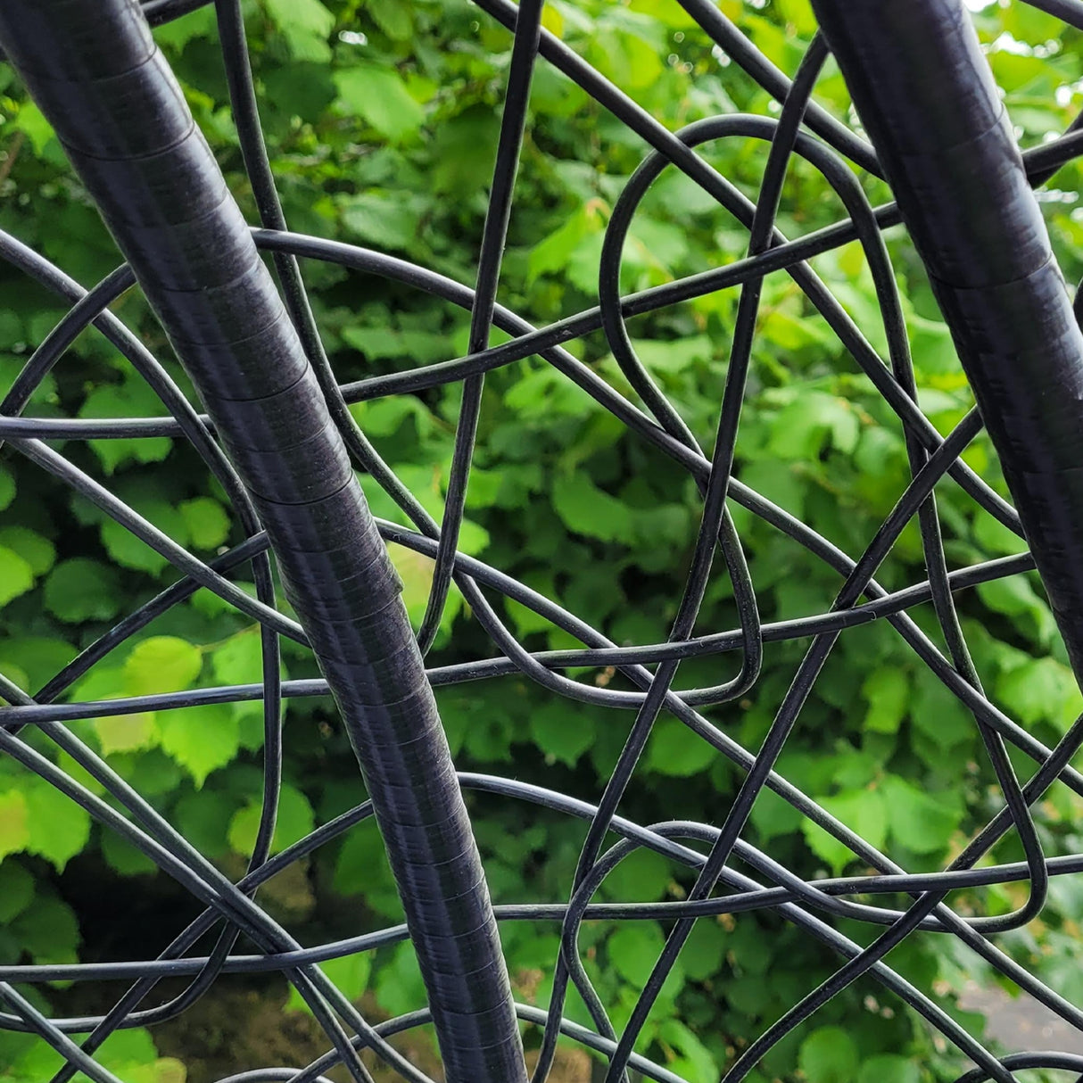 Struttura in rattan nero della sedia sospesa a uovo, con dettagli intrecciati e sfondo verde di foglie rigogliose