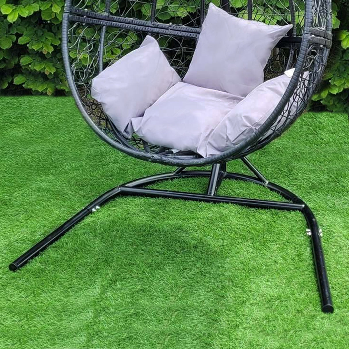 Sedia sospesa a uovo da giardino in rattan nero, con cuscini morbidi grigi, posizionata su erba verde brillante