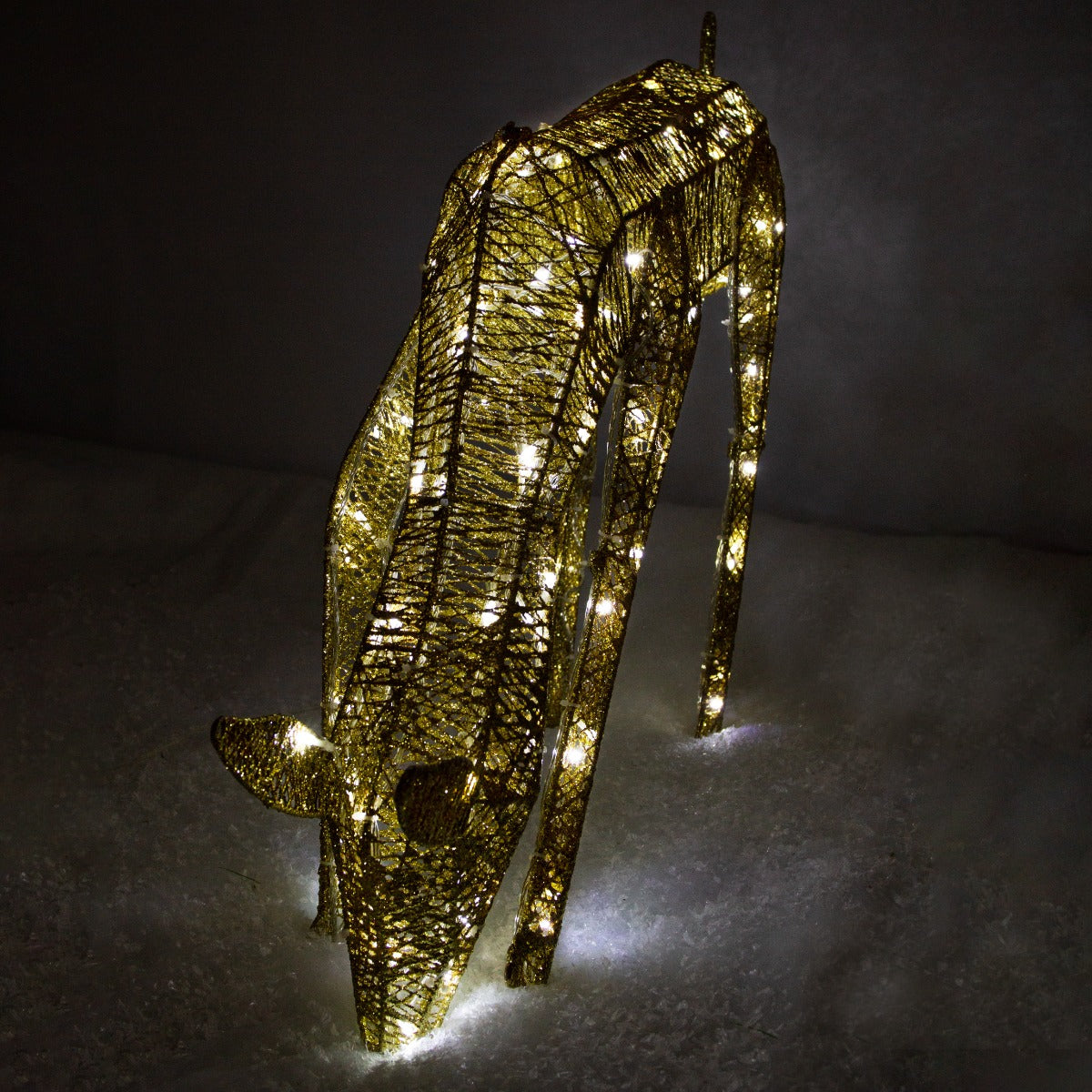 Renna di Natale femmina luminosa in oro, con dettagli metallici e luci bianche che brillano su un fondo bianco simile a neve