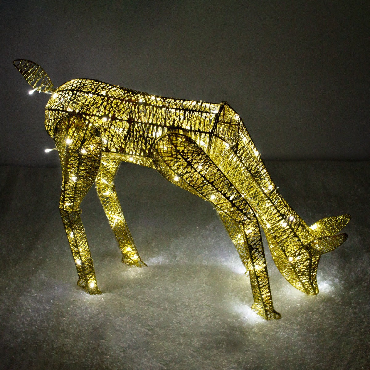 Renna di Natale femmina luminosa in oro, con dettagli intrecciati e luci LED che brillano, posizionata su uno sfondo bianco morbido