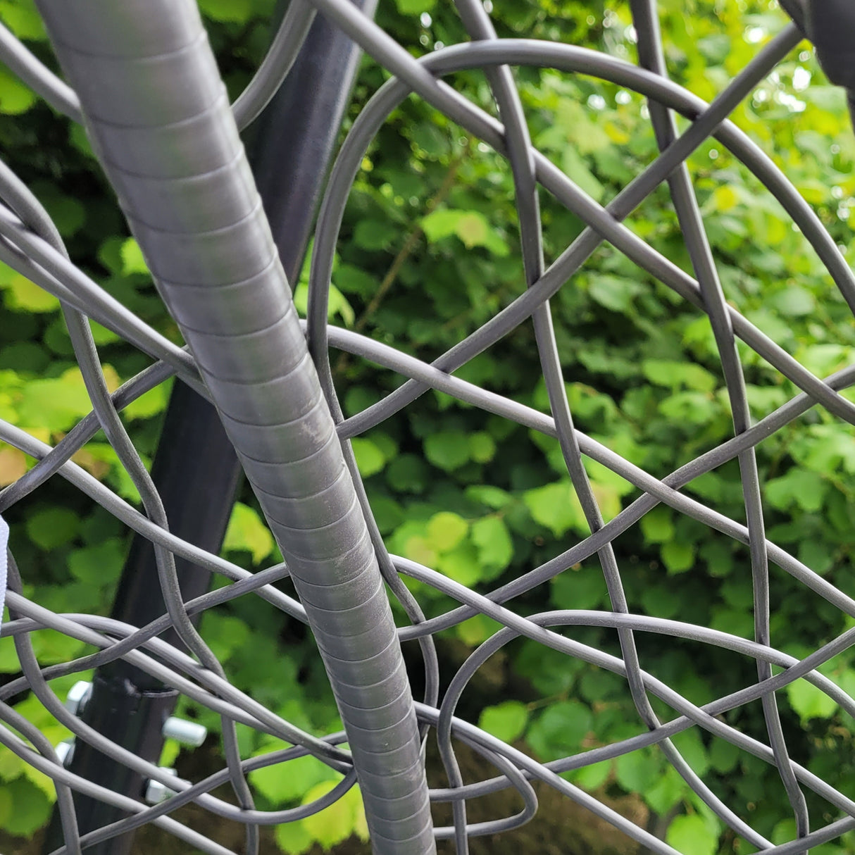Dettaglio della sedia sospesa a uovo in rattan grigio, con intrecci eleganti e struttura resistente, immersa nel verde del giardino