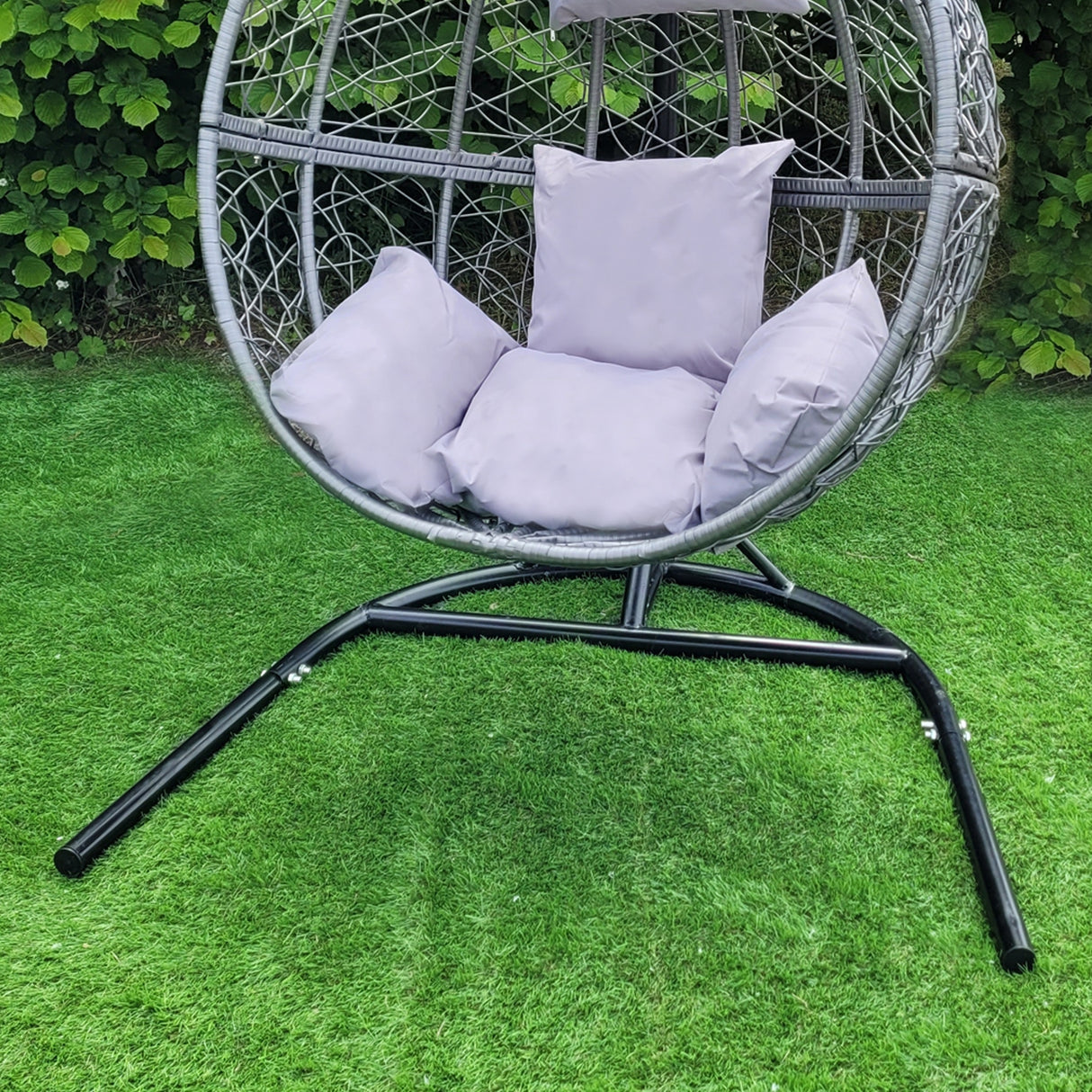 Sedia sospesa a uovo da giardino in rattan grigio, con cuscini morbidi e struttura nera, ideale per relax all'aperto