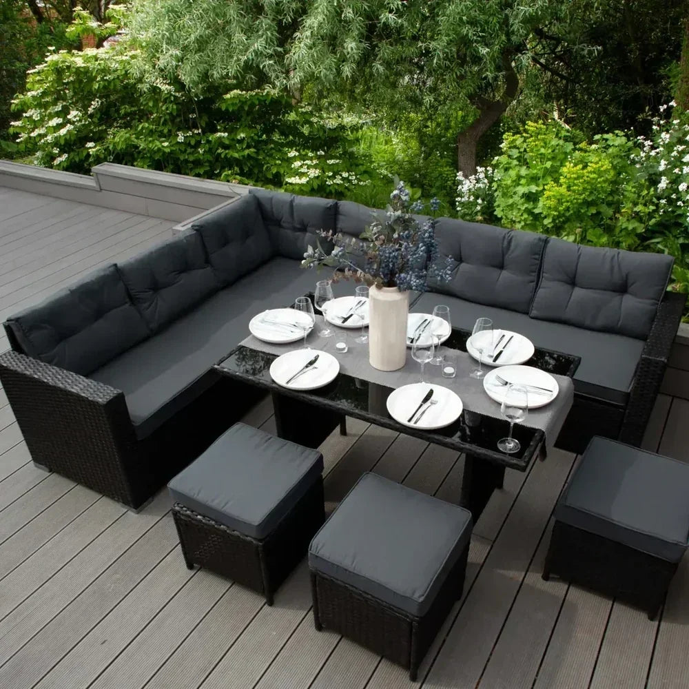 Set di mobili da giardino in rattan nero con cuscini grigi, tavolo elegante e stoviglie pronte per una cena all'aperto