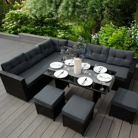 Set di mobili da giardino in rattan nero con cuscini grigi, tavolo elegante e stoviglie pronte per una cena all'aperto