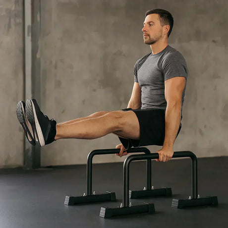 Uomo in maglietta grigia esegue un esercizio di sollevamento su parallele nere in un ambiente minimalista e moderno