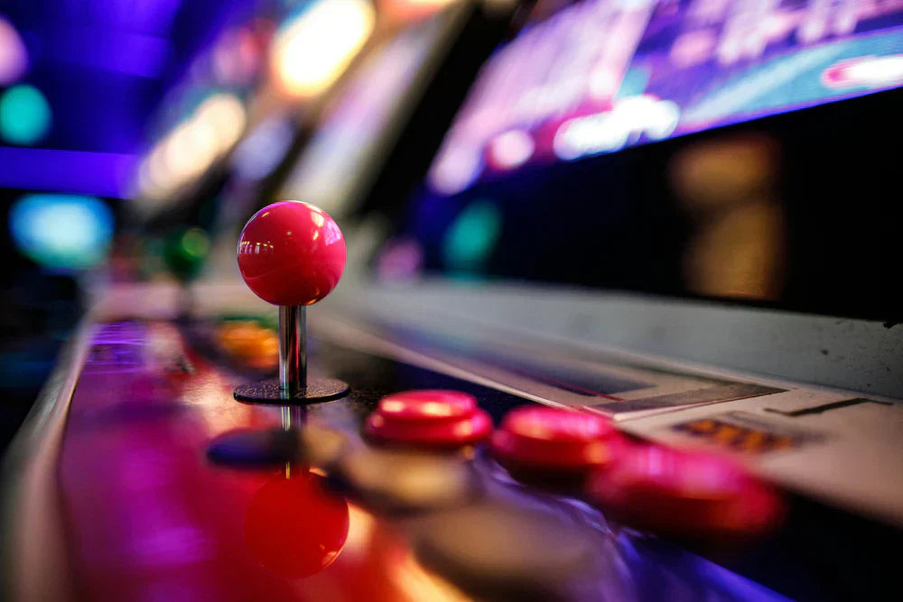 Pannello di una console arcade con un joystick rosa lucido e pulsanti colorati, sfondo sfocato di luci vivaci e retro illuminato