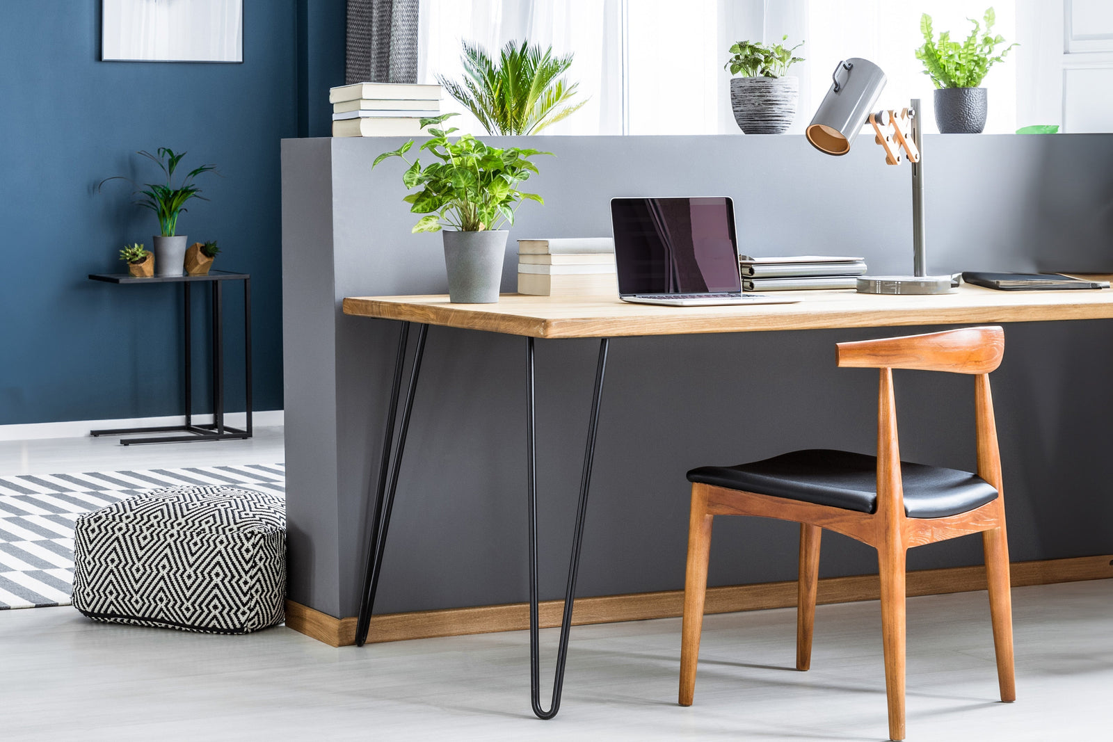 Scrivania in legno chiaro con gambe a forcina nere, sedia in legno con seduta nera, piante decorative e lampada moderna sul tavolo