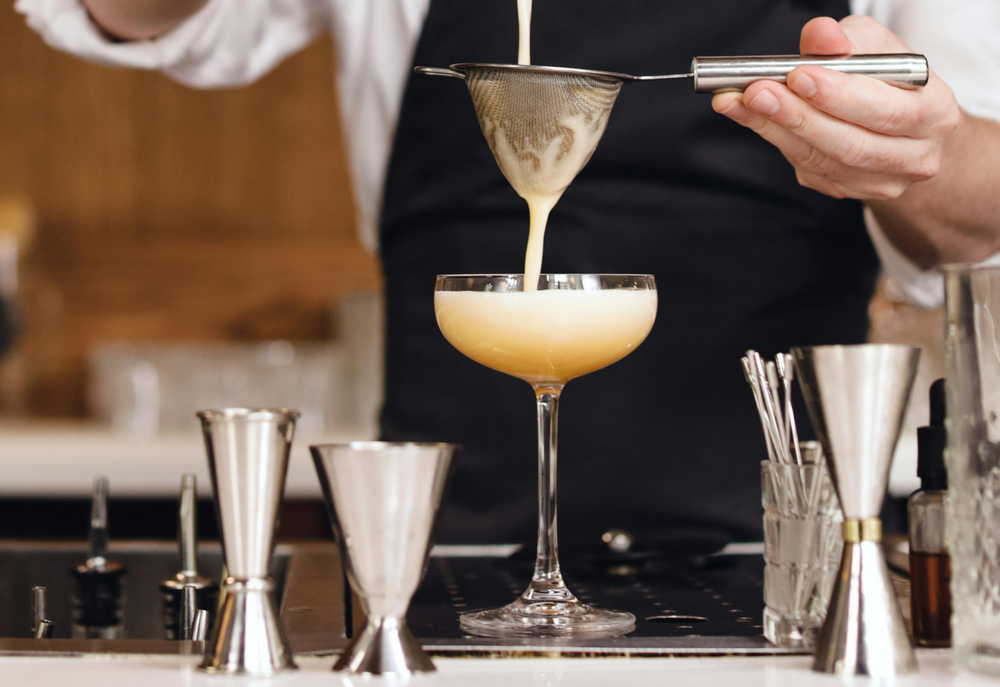 Barman versa un cocktail cremoso in un elegante bicchiere da cocktail, con attrezzature da bar in acciaio inox sullo sfondo