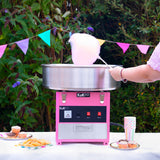 Macchina per zucchero filato KuKò, colore rosa, con una ciotola metallica lucida, circondata da dolci e festoni colorati all'aperto