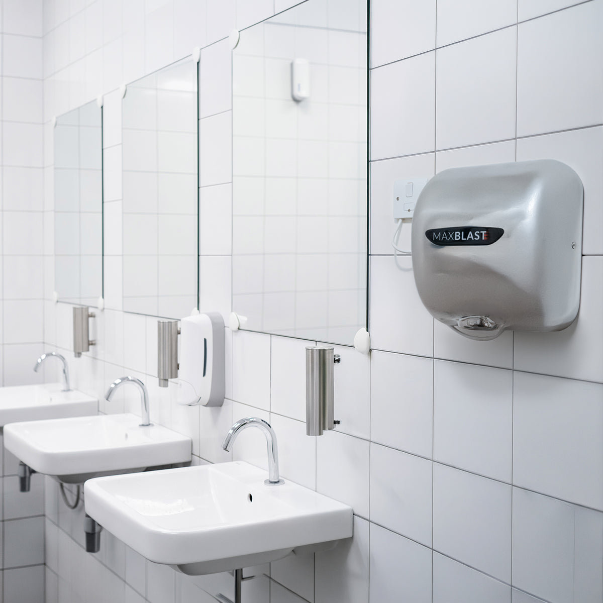Asciugamani elettrici MaxBlast grigi, specchi e lavandini bianchi in un bagno moderno con piastrelle bianche lucide