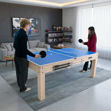 Tavolo giochi 7-in-1 beige con superficie blu, due panche contenitore, utilizzato da una coppia per giocare a ping pong in un soggiorno moderno