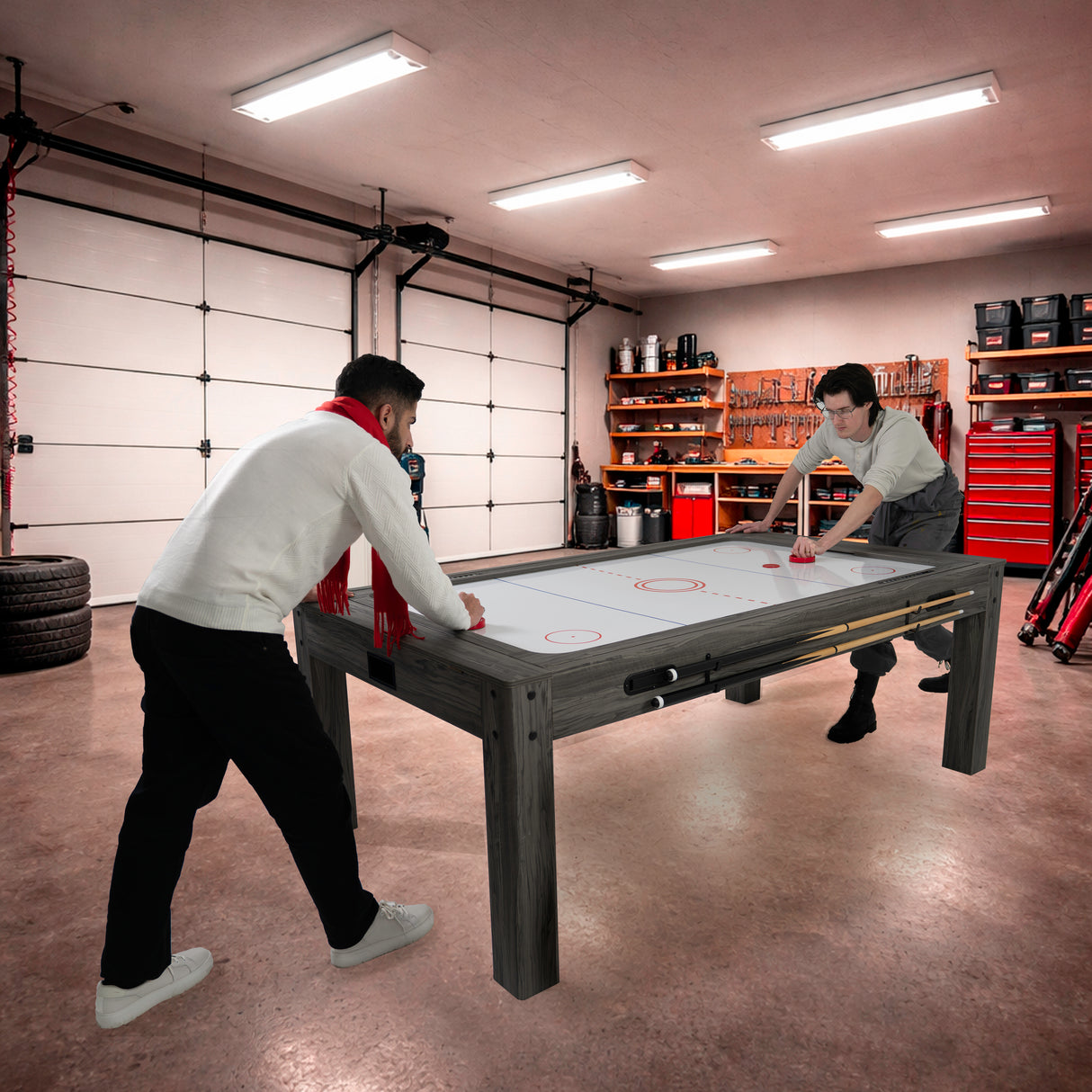 Tavolo giochi 7-in-1 grigio con due panche contenitore, utilizzato da due persone in un garage ben attrezzato, atmosfera vivace