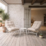 Due comode poltrone beige con cuscini morbidi su una terrazza in legno, accanto a un tavolino bianco e piante verdi in vaso