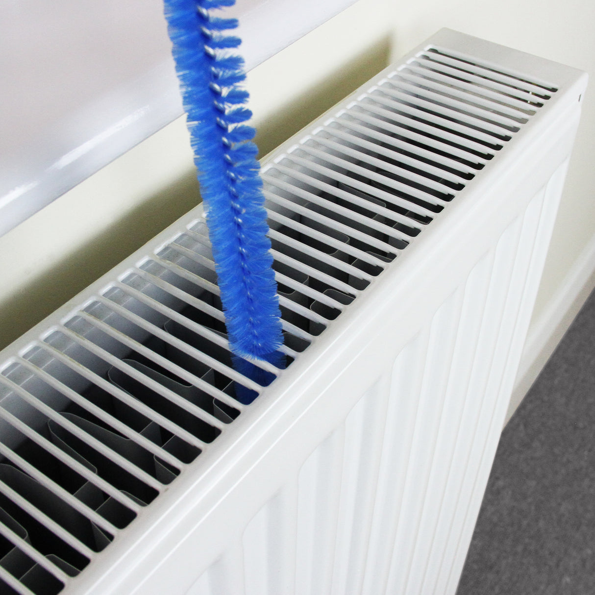 Copritermosifone in MDF bianco, lungo 1720mm, con griglia a lamelle e spazzola blu per la pulizia, su sfondo neutro