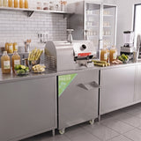 Pressa per canna da zucchero in acciaio inox, circondata da bottiglie di succhi e ingredienti freschi su un bancone moderno e luminoso