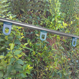 Serra 6x6 piedi con struttura in metallo grigio, base robusta e supporti blu, circondata da foglie verdi e vegetazione lussureggiante