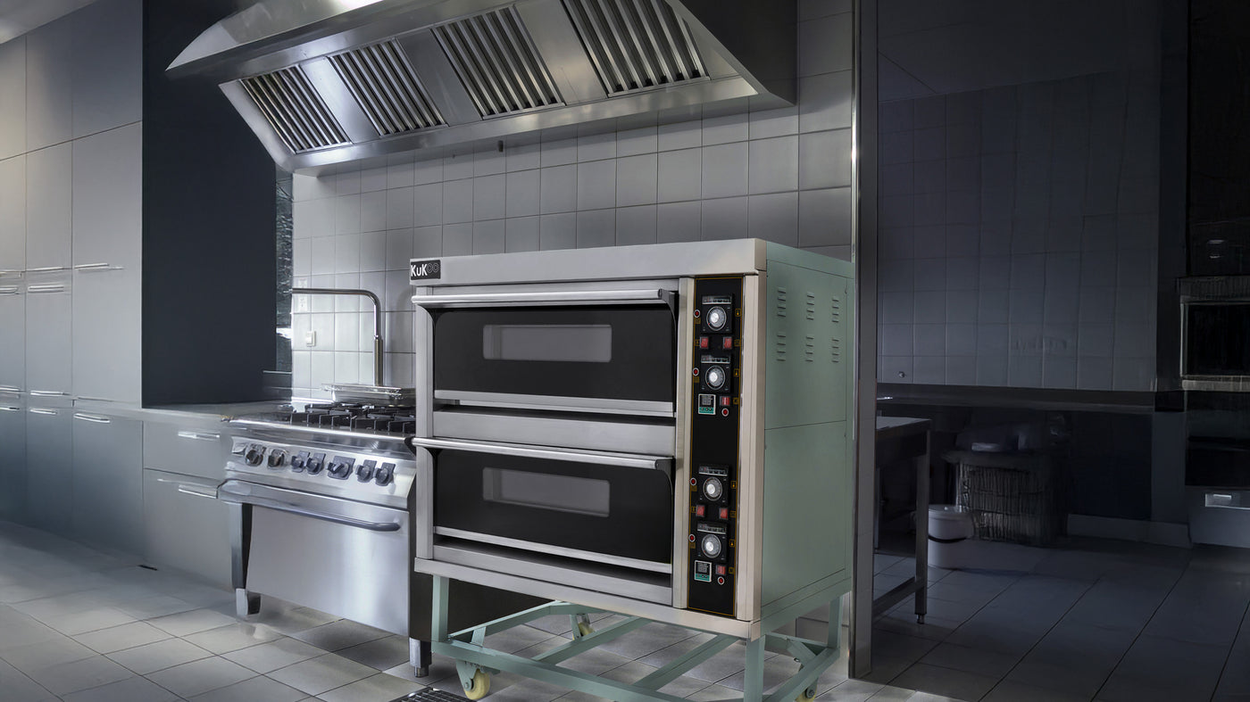 Forno a doppia camera in acciaio inox con manopole nere, posizionato in una cucina moderna con pareti grigie e attrezzature professionali