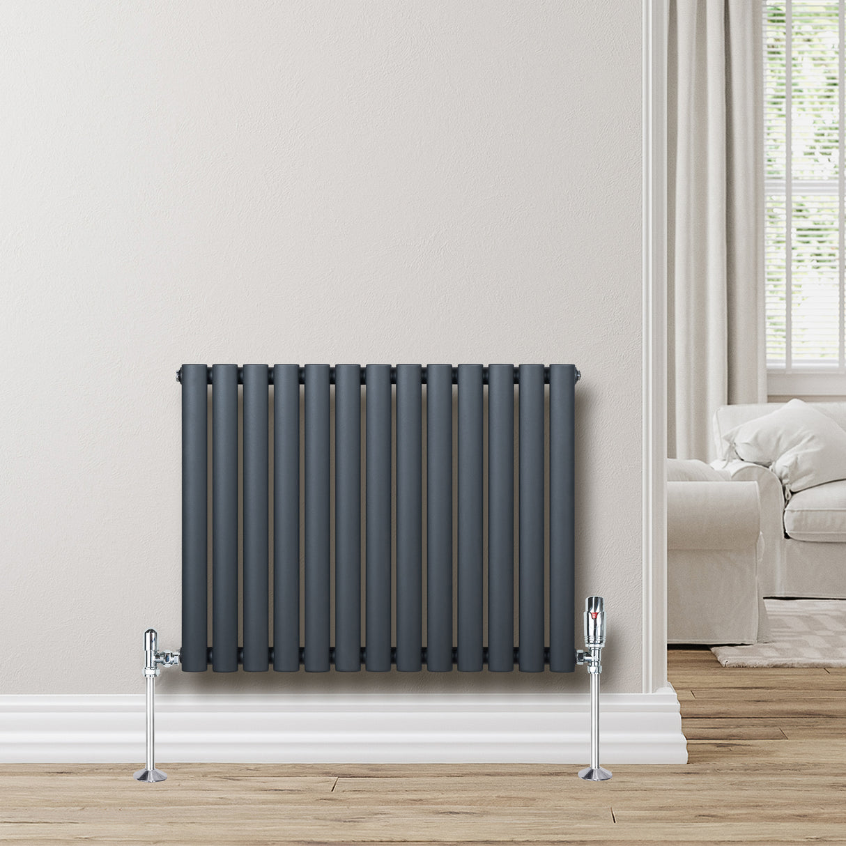 Radiatore ovale a colonna singola orizzontale antracite, con valvole, installato su parete chiara in ambiente moderno e luminoso