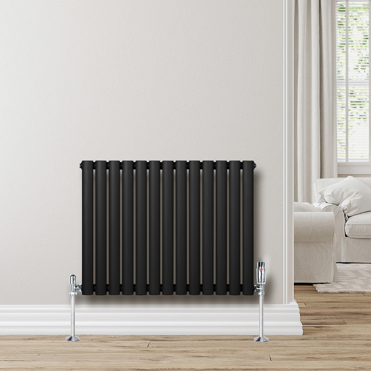 Radiatore ovale a colonna singola orizzontale nero, con valvole cromate, posizionato su una parete chiara in un ambiente moderno e luminoso