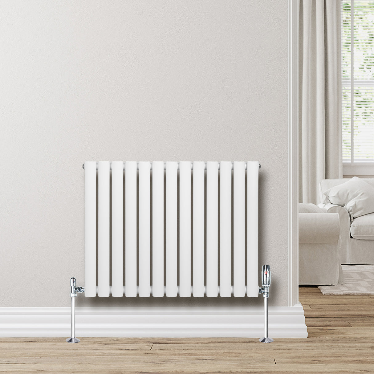 Radiatore ovale a colonna singola orizzontale bianco, con valvole cromate, posizionato su un pavimento in legno chiaro vicino a una finestra