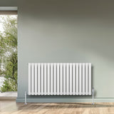 Radiatore ovale a colonna singola orizzontale bianco, 600 x 1200 mm, con valvole, posizionato su un pavimento in legno chiaro vicino a una finestra
