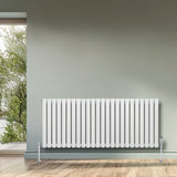 Radiatore ovale a colonna singola orizzontale bianco, con finitura liscia e valvole, installato su parete grigia in ambiente luminoso
