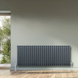 Radiatore ovale a colonna singola orizzontale antracite, 600 x 1620 mm, con valvole, posizionato su parete chiara e pavimento in legno
