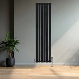 Radiatore piatto monocolonna nero, 1600 x 420 mm, con finitura liscia e valvole cromate, posizionato in un ambiente moderno con piante verdi