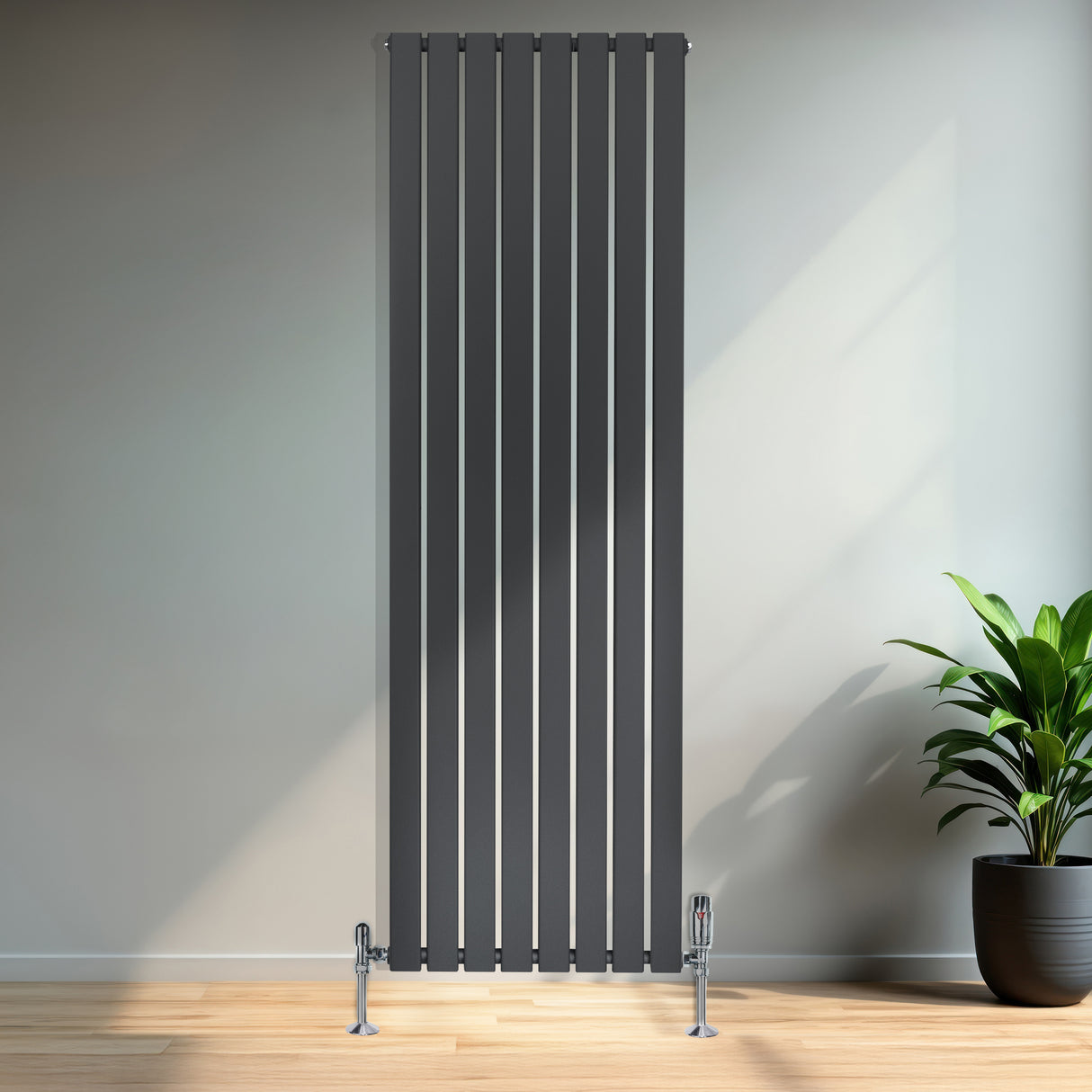 Radiatore piatto monocolonna grigio antracite, alto e stretto, con finitura liscia e valvole, posizionato in un ambiente moderno con piante verdi