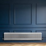 Radiatore tradizionale a 4 colonne, bianco lucido, installato su una parete blu scuro, con pavimento in legno chiaro elegante