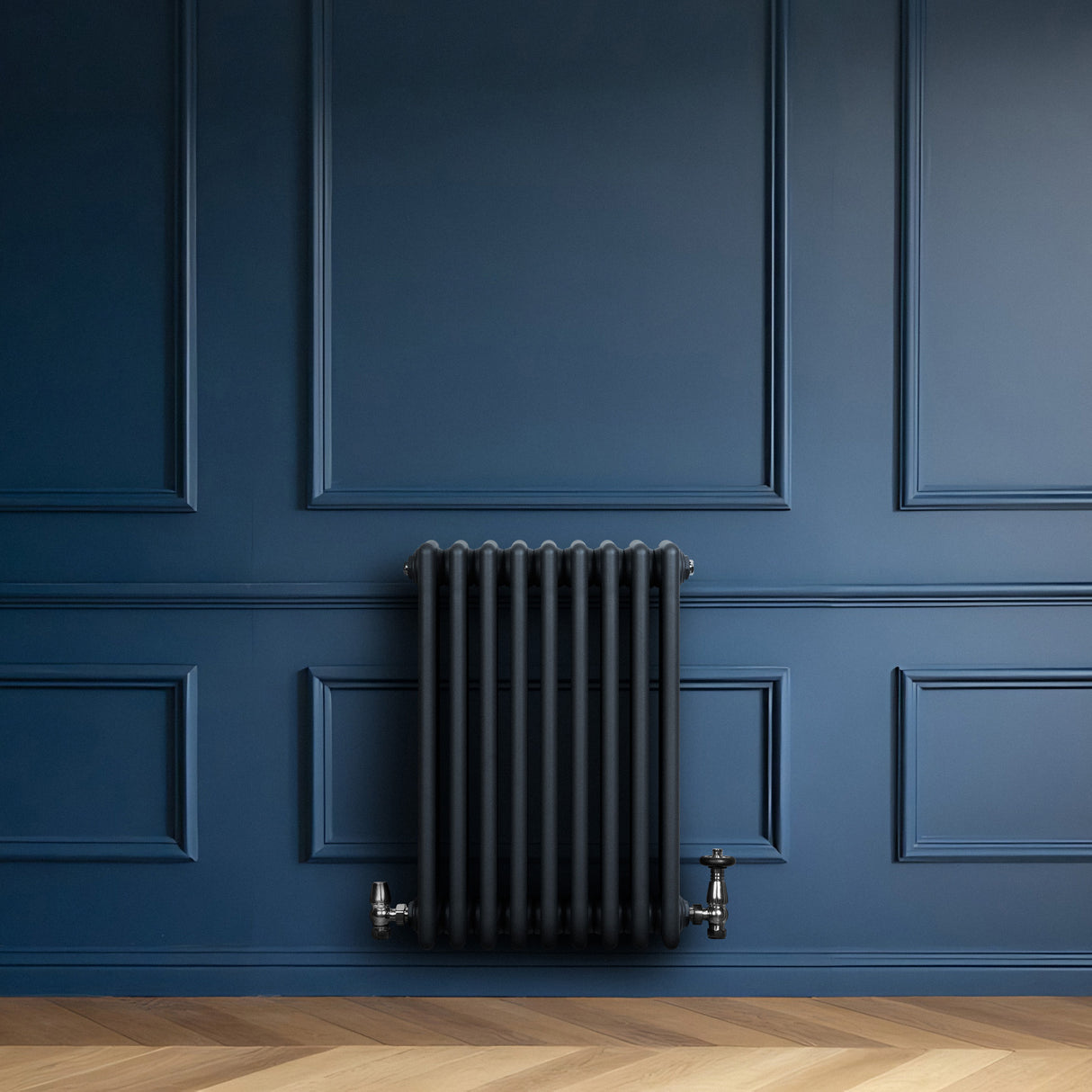 Radiatore tradizionale a 4 colonne in grigio antracite, installato su una parete blu, con valvole metalliche lucide e finitura liscia