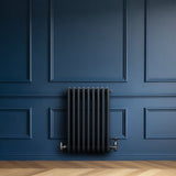 Radiatore tradizionale a 4 colonne in grigio antracite, installato su una parete blu, con valvole metalliche lucide e finitura liscia