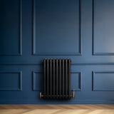 Radiatore tradizionale a 4 colonne in nero, installato su parete blu, con valvole in ottone e pavimento in legno chiaro