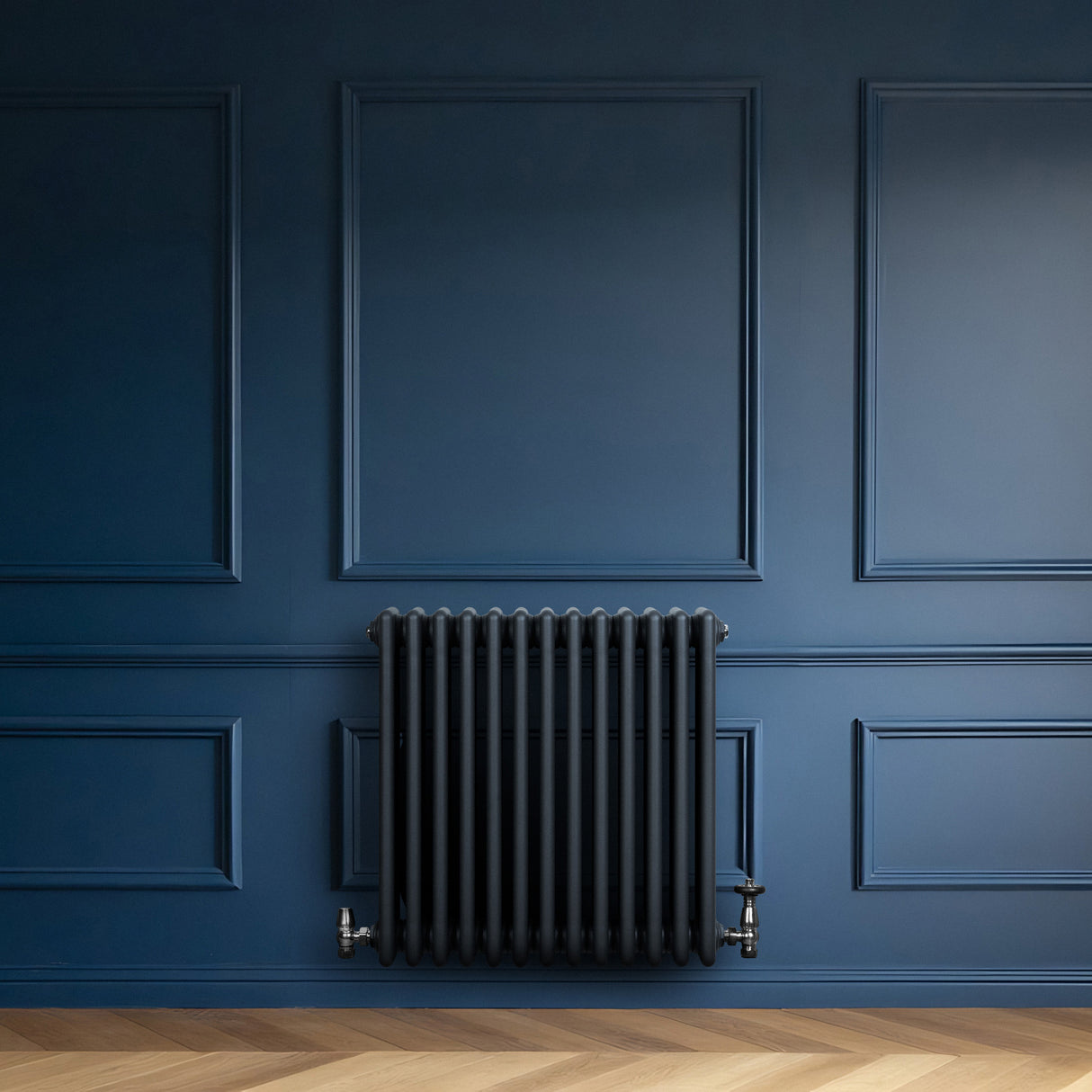 Radiatore tradizionale a 4 colonne grigio antracite montato su parete blu, con valvole metalliche e design elegante e moderno