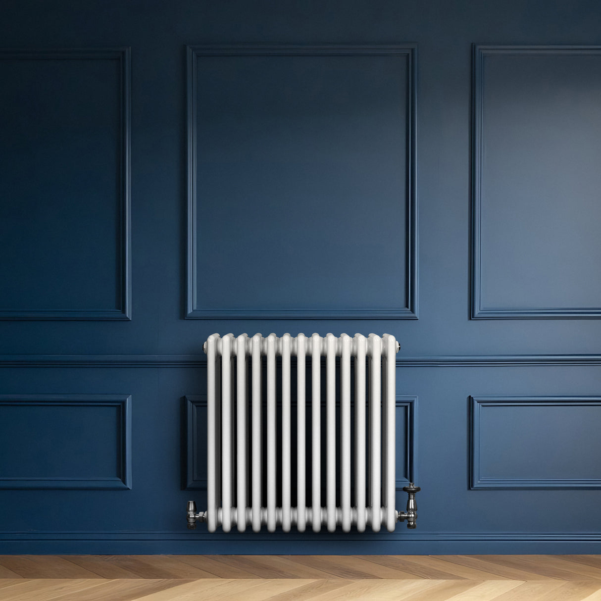 Radiatore tradizionale a 4 colonne, bianco, con valvole, posizionato su una parete blu scuro, su un pavimento in legno chiaro