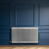 Radiatore tradizionale bianco a 4 colonne orizzontali, installato su una parete blu, con valvole metalliche lucide e finitura liscia