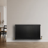 Radiatore tradizionale orizzontale a 4 colonne, finitura nera lucida, installato su parete bianca con valvole dorate, design elegante e moderno