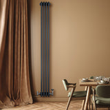 Radiatore tradizionale verticale a 4 colonne in grigio antracite, installato su parete beige, con valvole e arredamento elegante in legno e tessuto