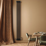Radiatore tradizionale verticale a 4 colonne, finitura nera opaca, installato su una parete beige, accanto a un tavolo elegante