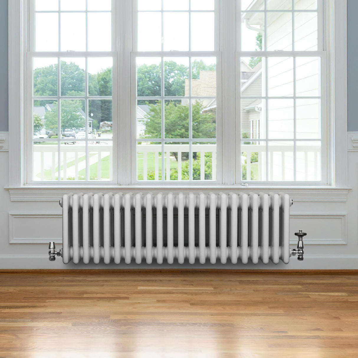 Radiatore tradizionale a 4 colonne bianco, installato sotto una finestra, con valvole e finitura liscia su pavimento in legno chiaro