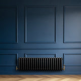 Radiatore tradizionale a 4 colonne, 300 x 1010 mm, finitura nera lucida, installato su parete blu, con dettagli in ottone